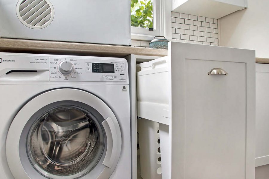 Compact laundry with shaker cabinets and pull out laundry basket and subway tiles