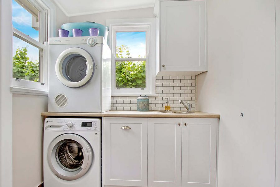 Compact laundry with shaker cabinets and pull out laundry basket and subway tiles