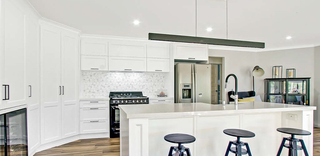 full shaker kitchen and island bench Kurrajong Shaker Kitchen with long white cupboards, black handles, white stone benchtop and island with undermount sink and breakfast bar